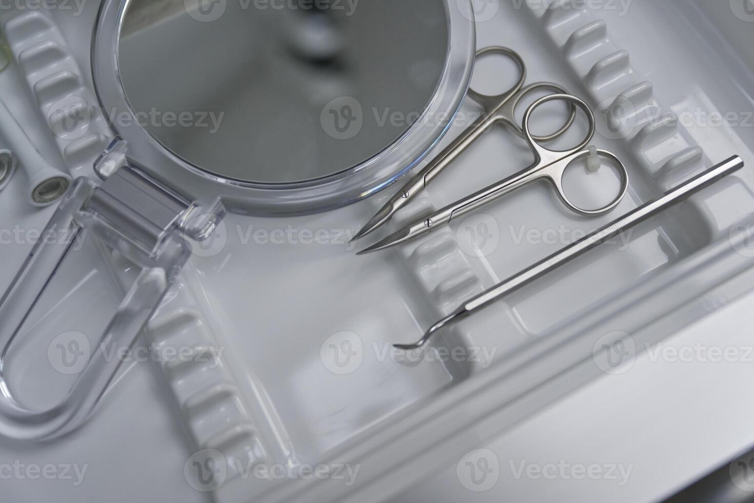 A close-up view of a medical tray containing surgical instruments, including scissors, tweezers, and a mirror, arranged neatly on a white surface. photo