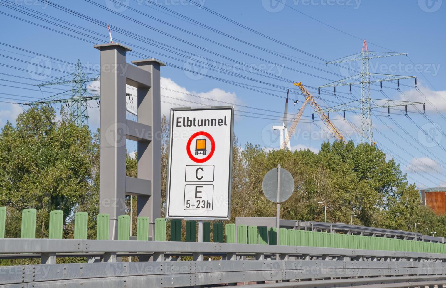 A road sign indicating the Elbtunnel with restrictions for vehicles. The sign shows a bus symbol and specifies operational hours from 5 to 23. In the background, there are power lines photo