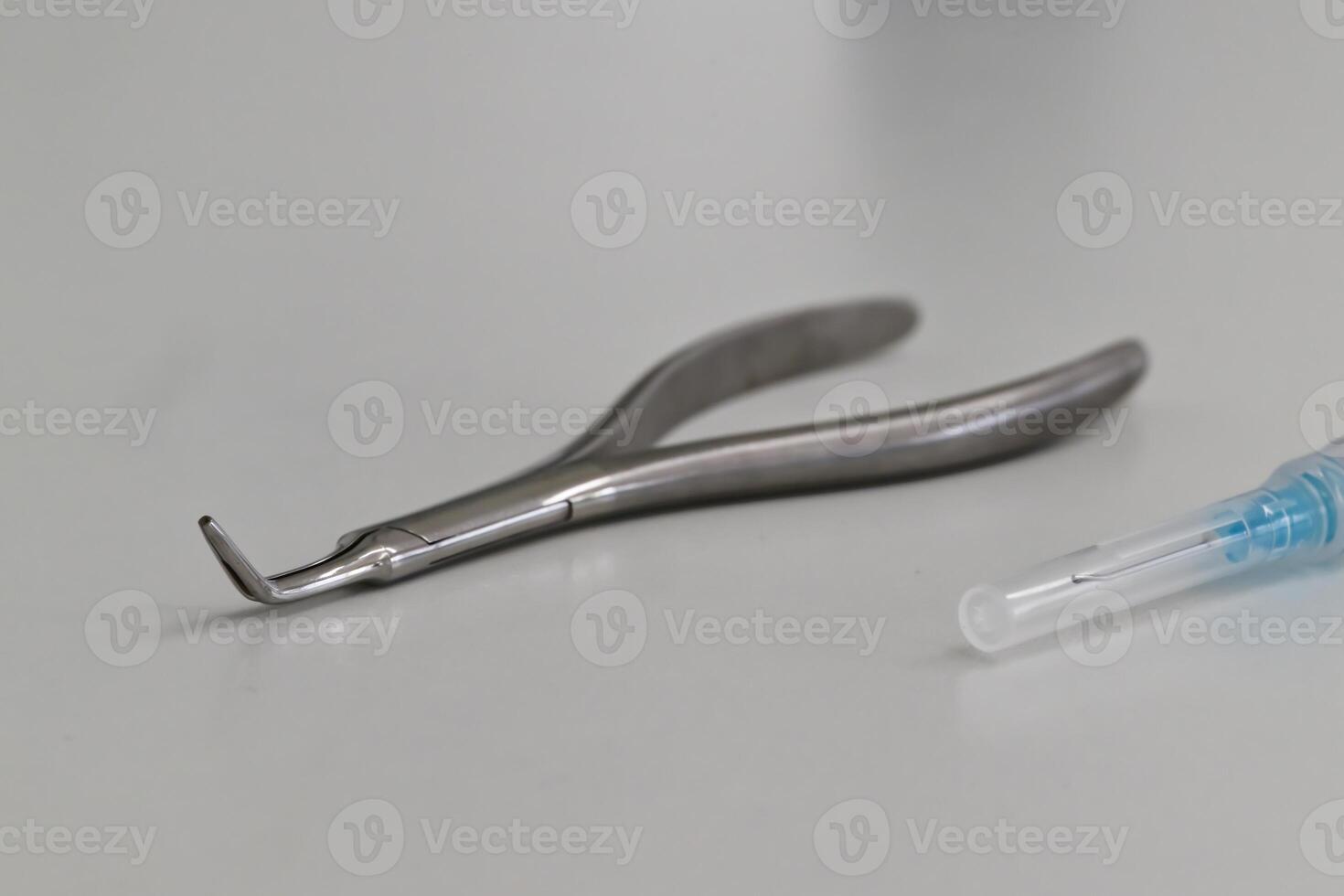 A close-up of a dental tool, specifically a dental explorer, alongside a syringe. The tools are made of stainless steel and are placed on a clean, white surface. photo