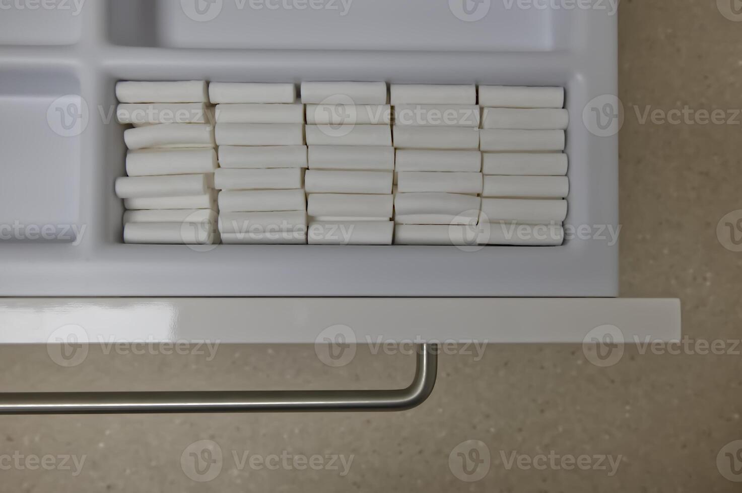 A neatly organized drawer containing rows of white cylindrical cotton rolls for dental use to separate lips from teeth.Neatly Organized Drawer with White Cylindrical Objects photo