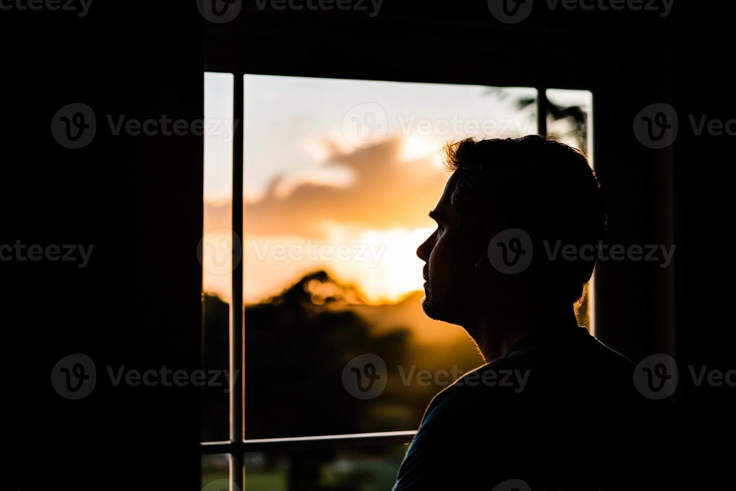 A man is looking out a window at the sunset photo