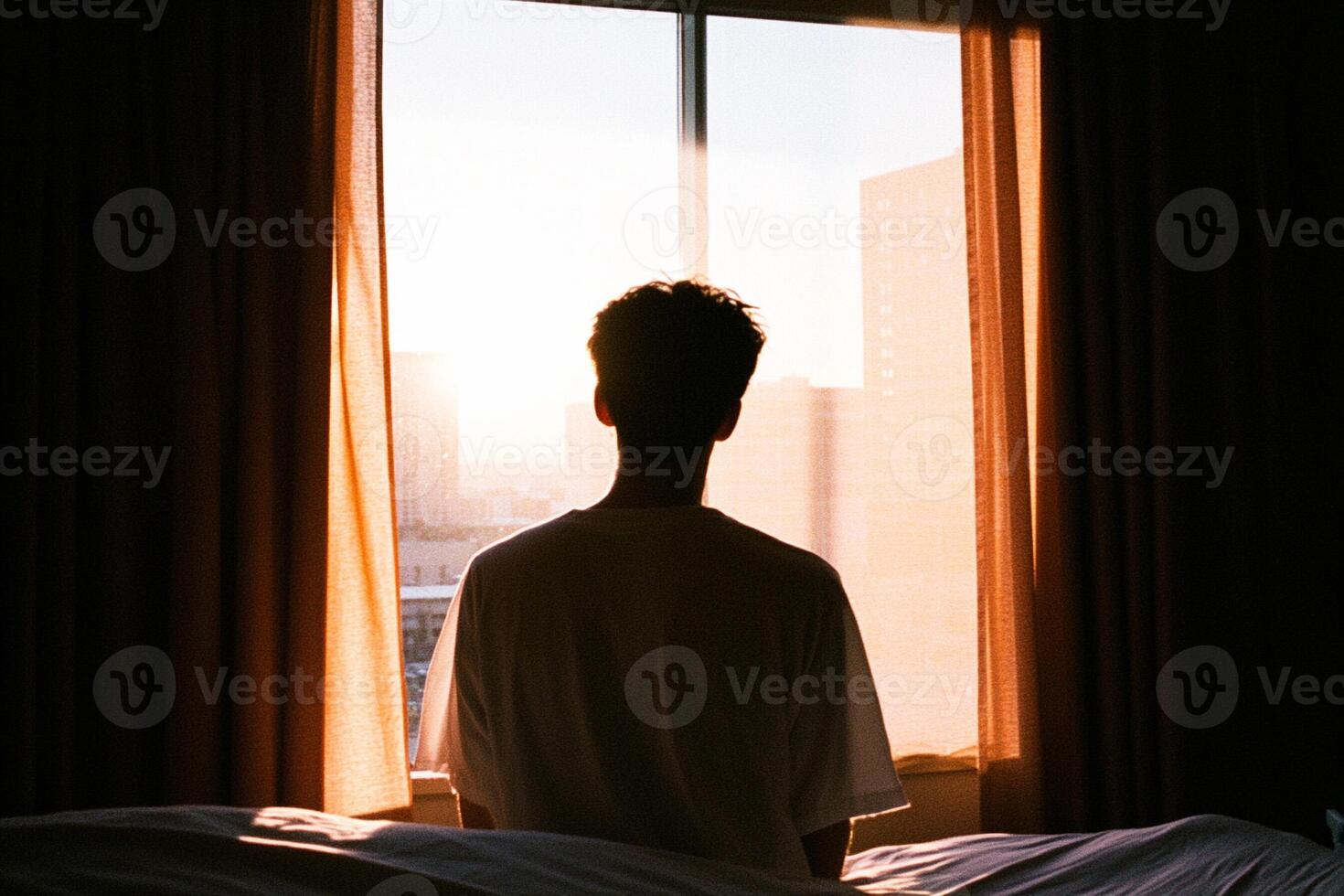 A man sitting in a bed looking out a window photo