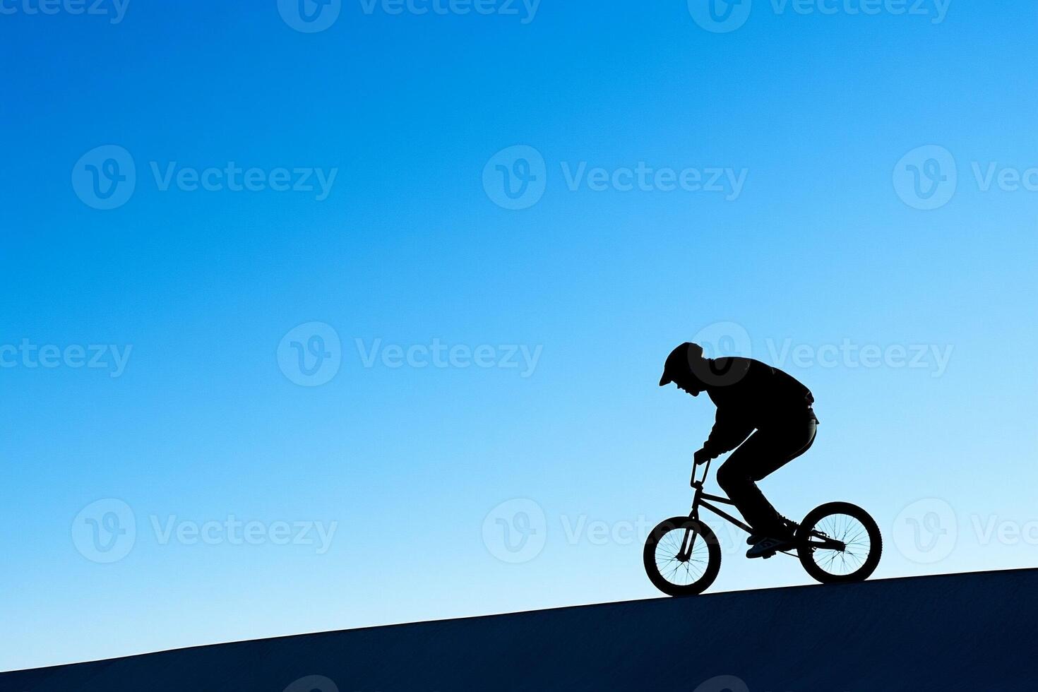 A silhouette of a person riding a bike on a hill photo