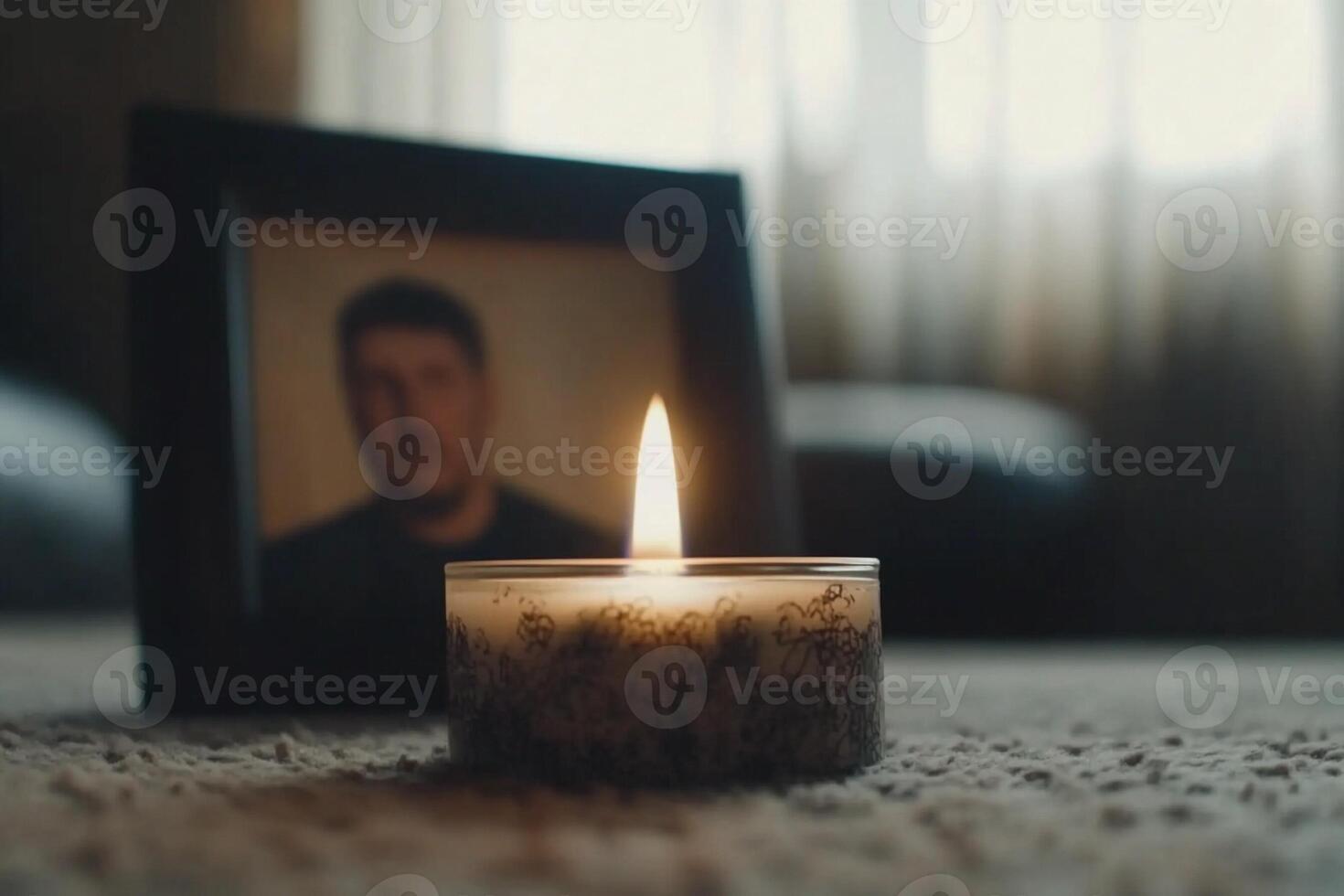 A candle sits on a carpet in front of a framed photo