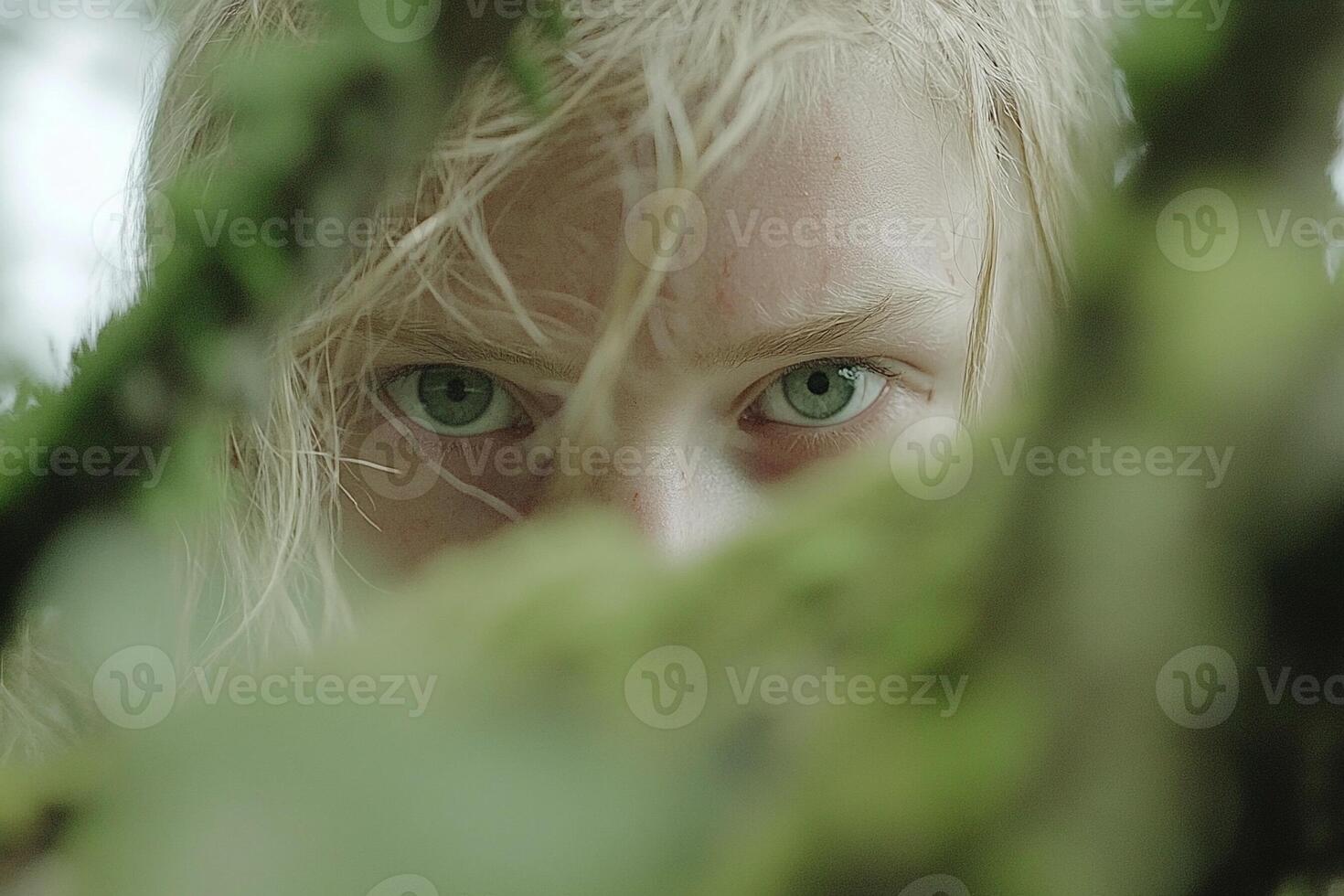 A young blonde woman peeking out from behind a tree photo