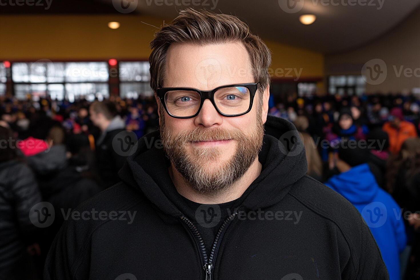 A man with glasses and a black jacket standing in front of a crowd photo