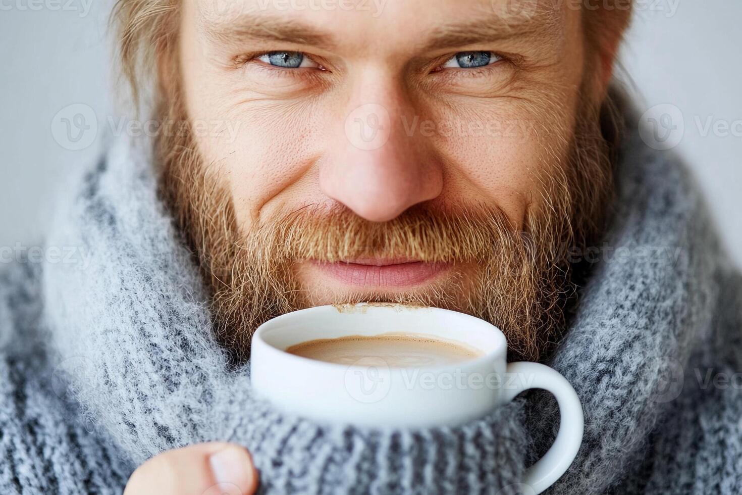 A man with a beard and sweater is holding a cup of coffee photo