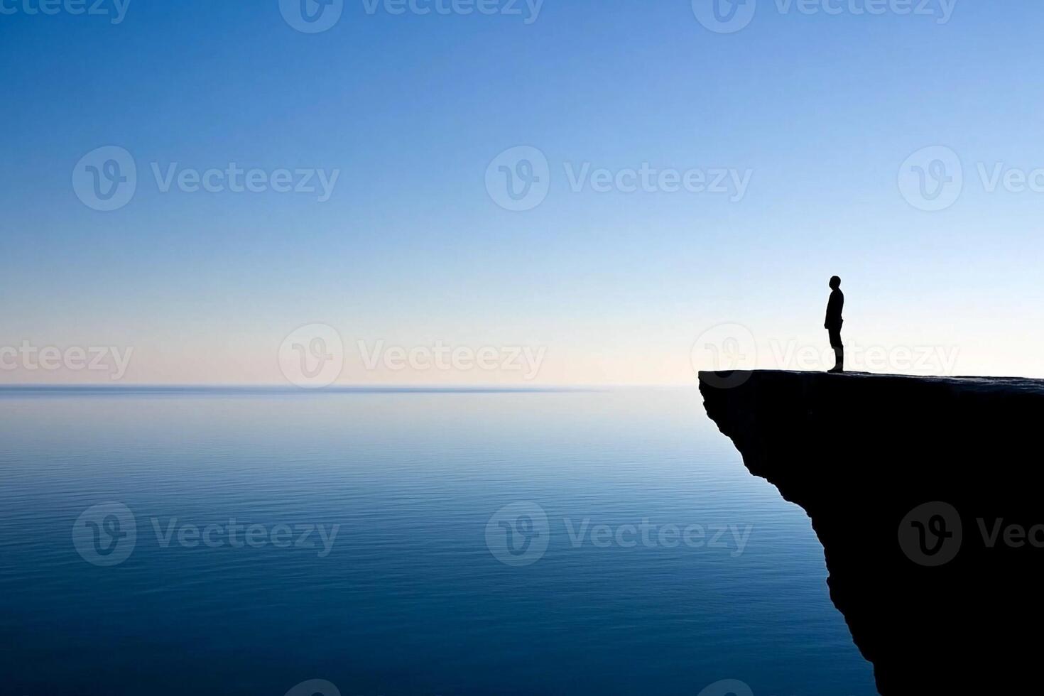 A man standing on the edge of a cliff overlooking the ocean photo