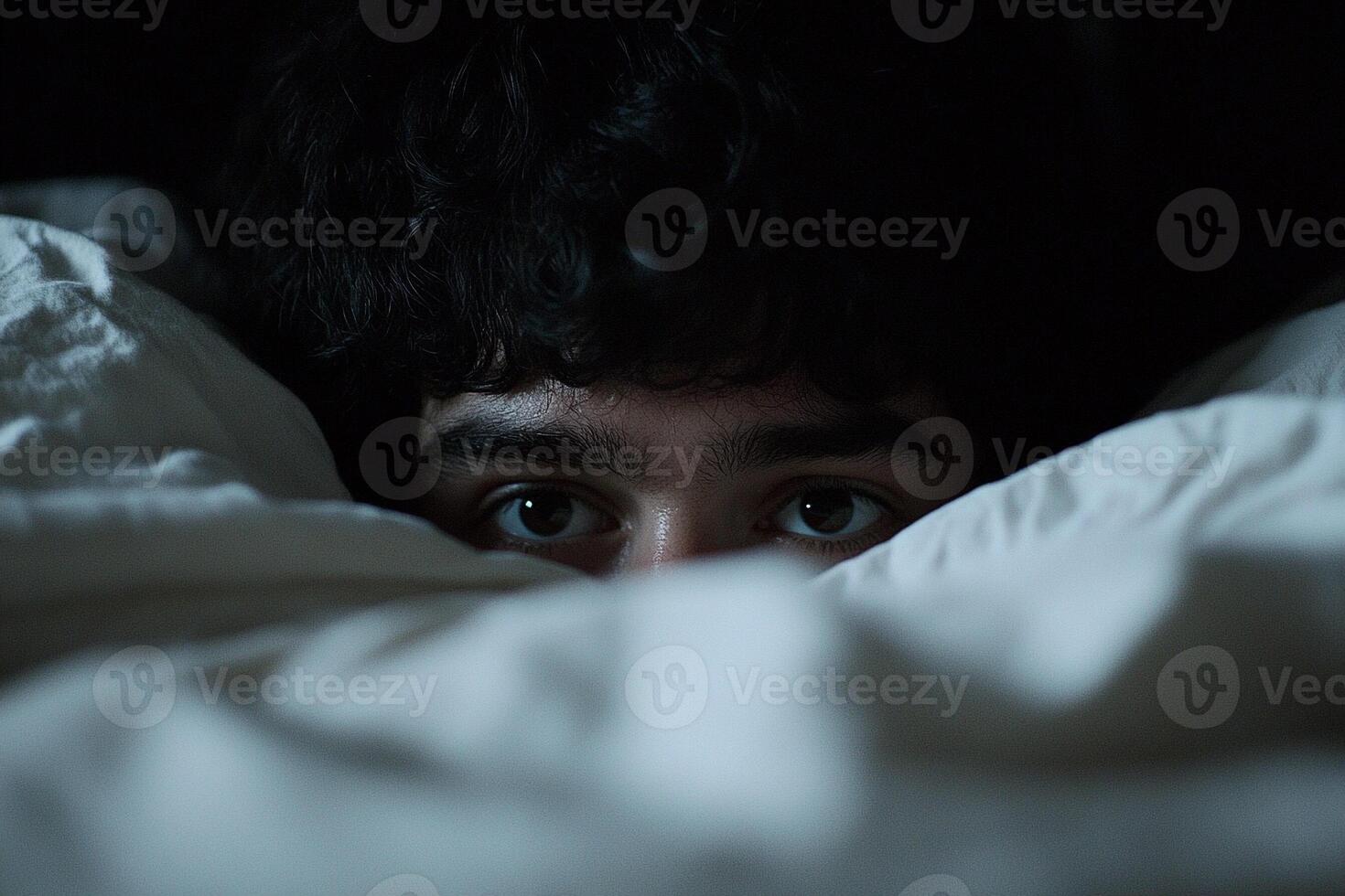 A young man peeking out from under a blanket photo