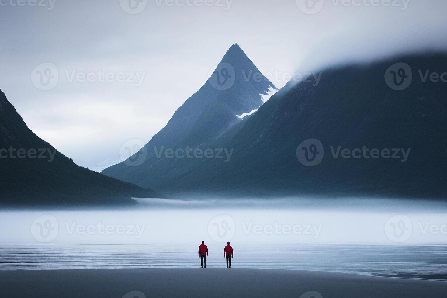 Two people in red jackets standing on the beach in front of mountains photo