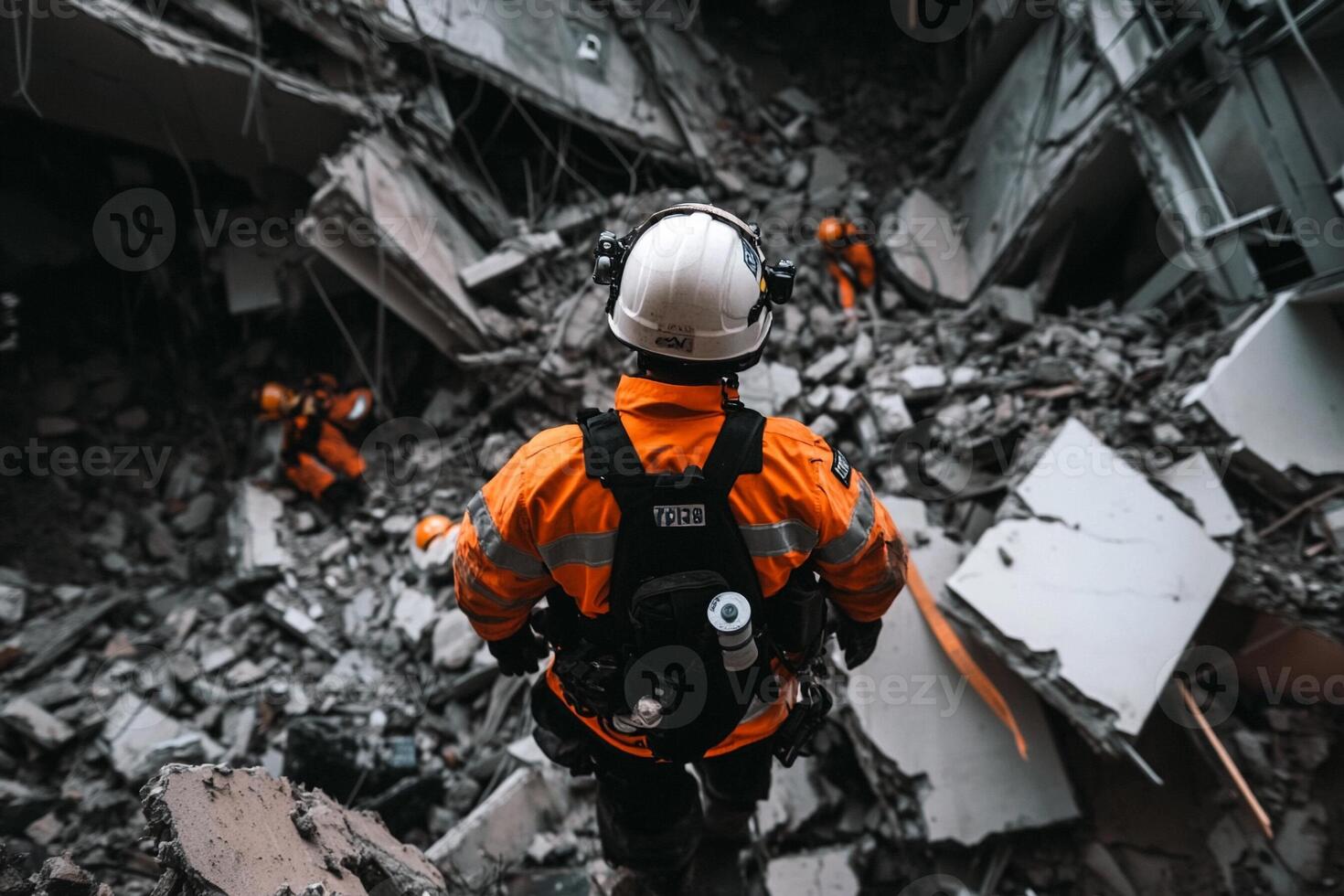 A man in an orange jacket and hard hat is walking through rubble photo