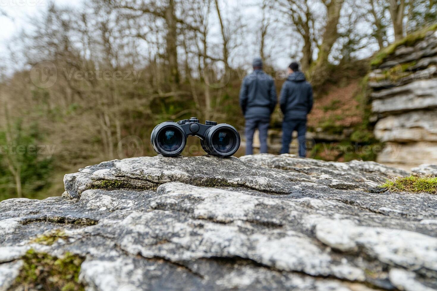 Two people looking at a pair of binoculars on a rock photo