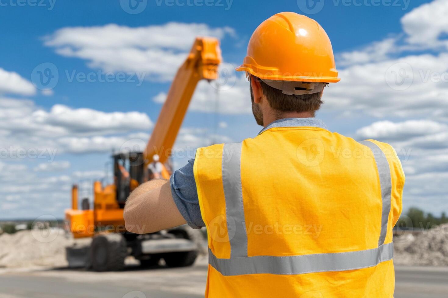 A man in an orange vest and hard hat is standing in front of a construction vehicle photo