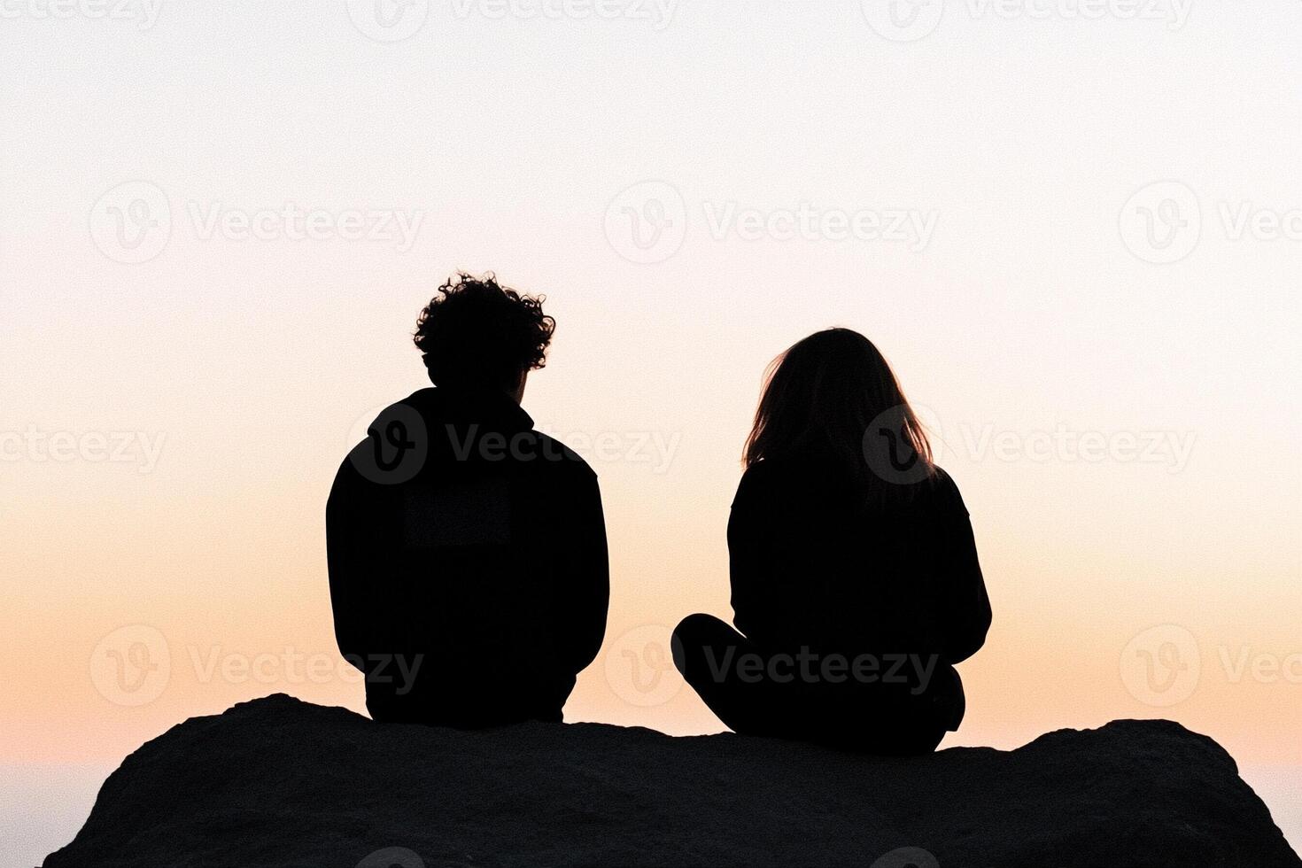 Two people sitting on top of a mountain at sunset photo