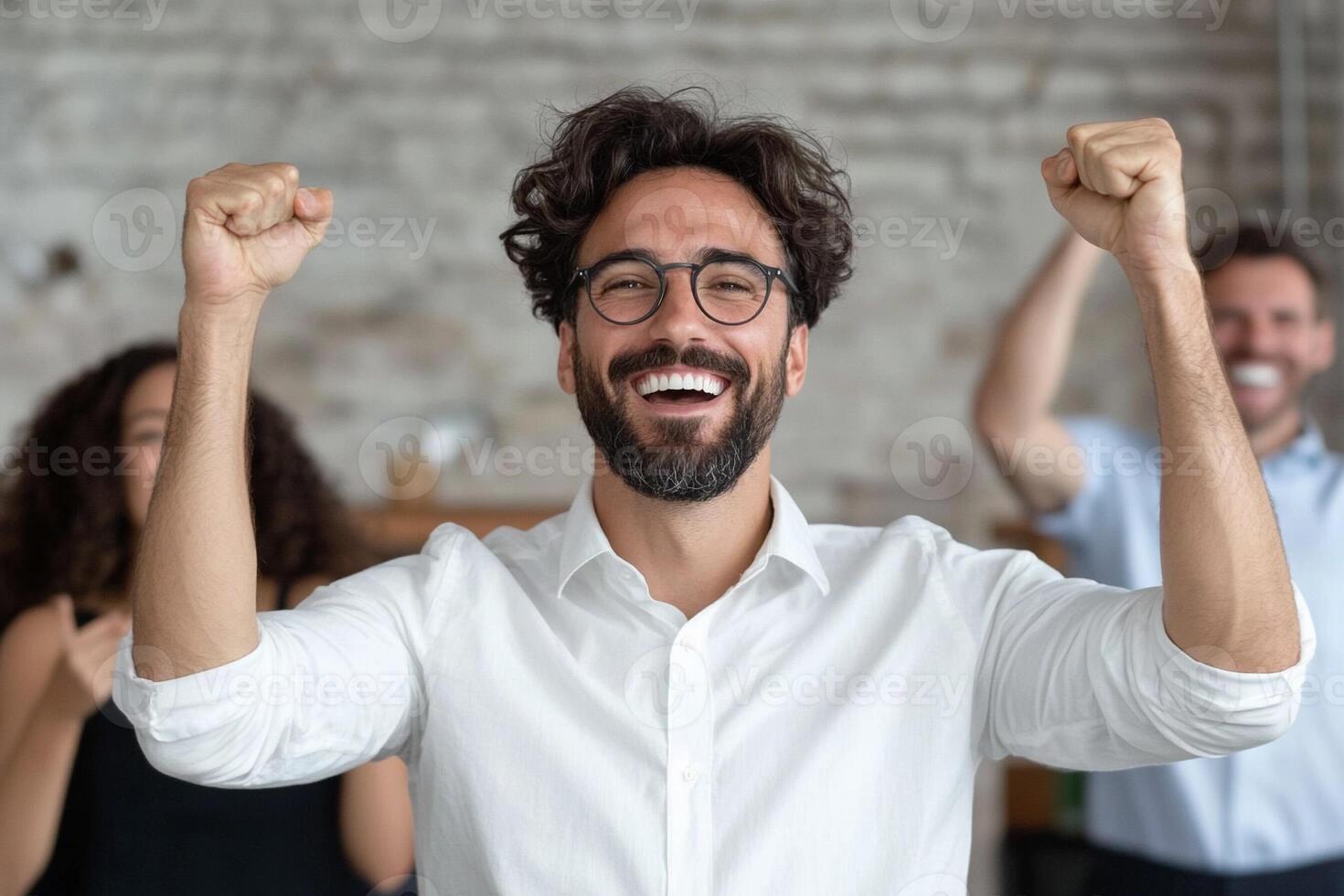 A man with glasses and a beard is celebrating with his arms up photo