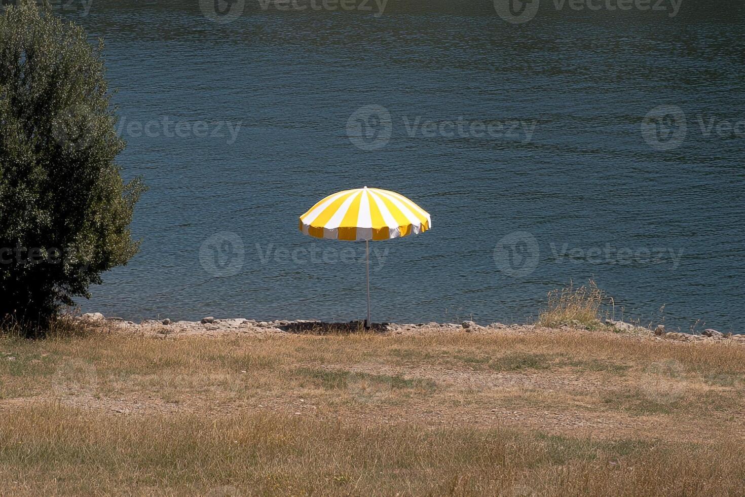 A yellow and white umbrella sitting on a hill overlooking the water photo
