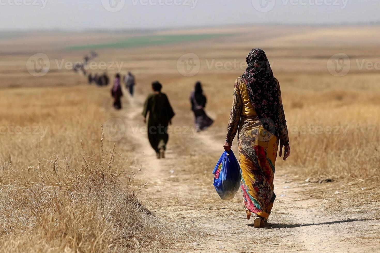 A woman walks along a dirt road in a dry field photo