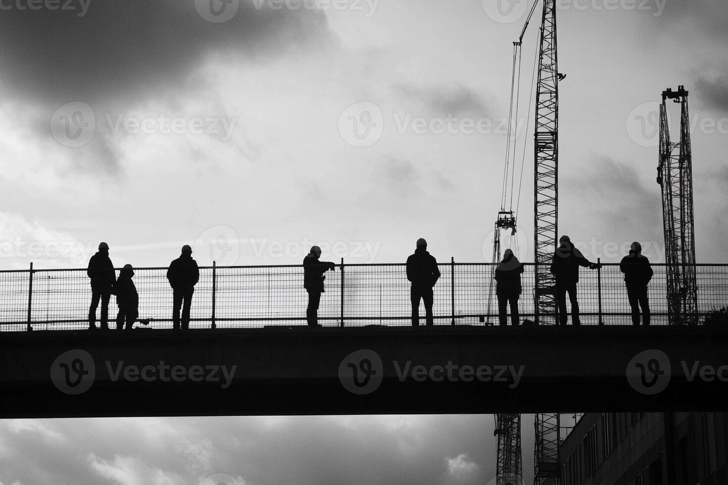 A group of people standing on a bridge with construction cranes in the background photo