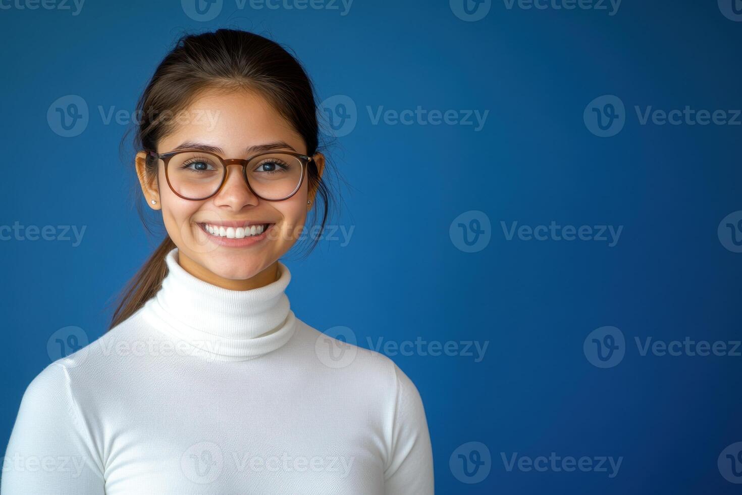 Portrait of a beautiful young woman wearing glasses and a turtle neck sweater on a blue background photo