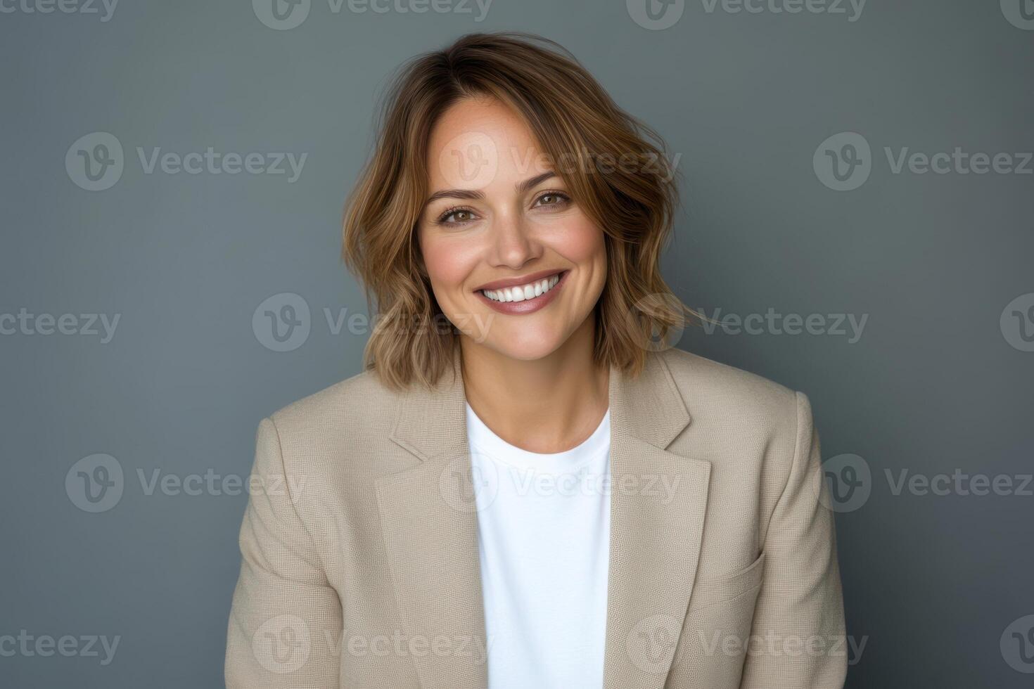 Professional portrait of a smiling woman in a beige blazer against a gray backdrop photo