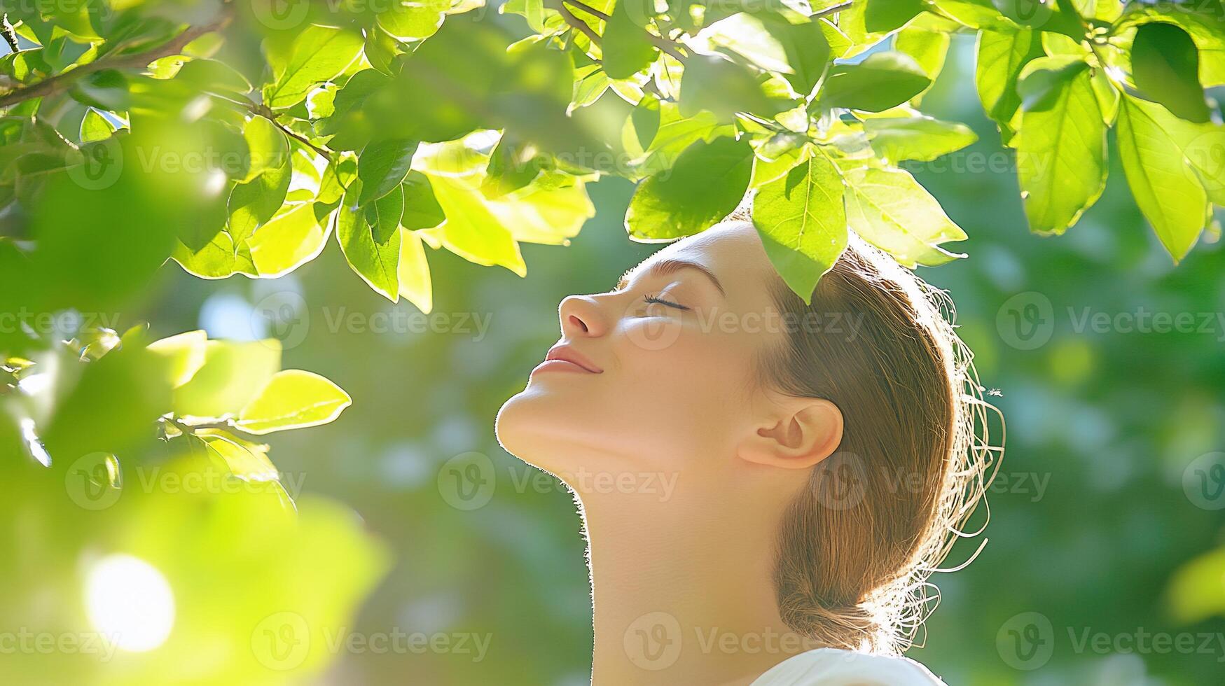 A woman is looking up at the sun through leaves photo