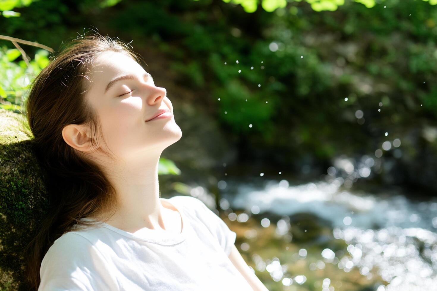 A woman is sitting by a stream with her eyes closed photo