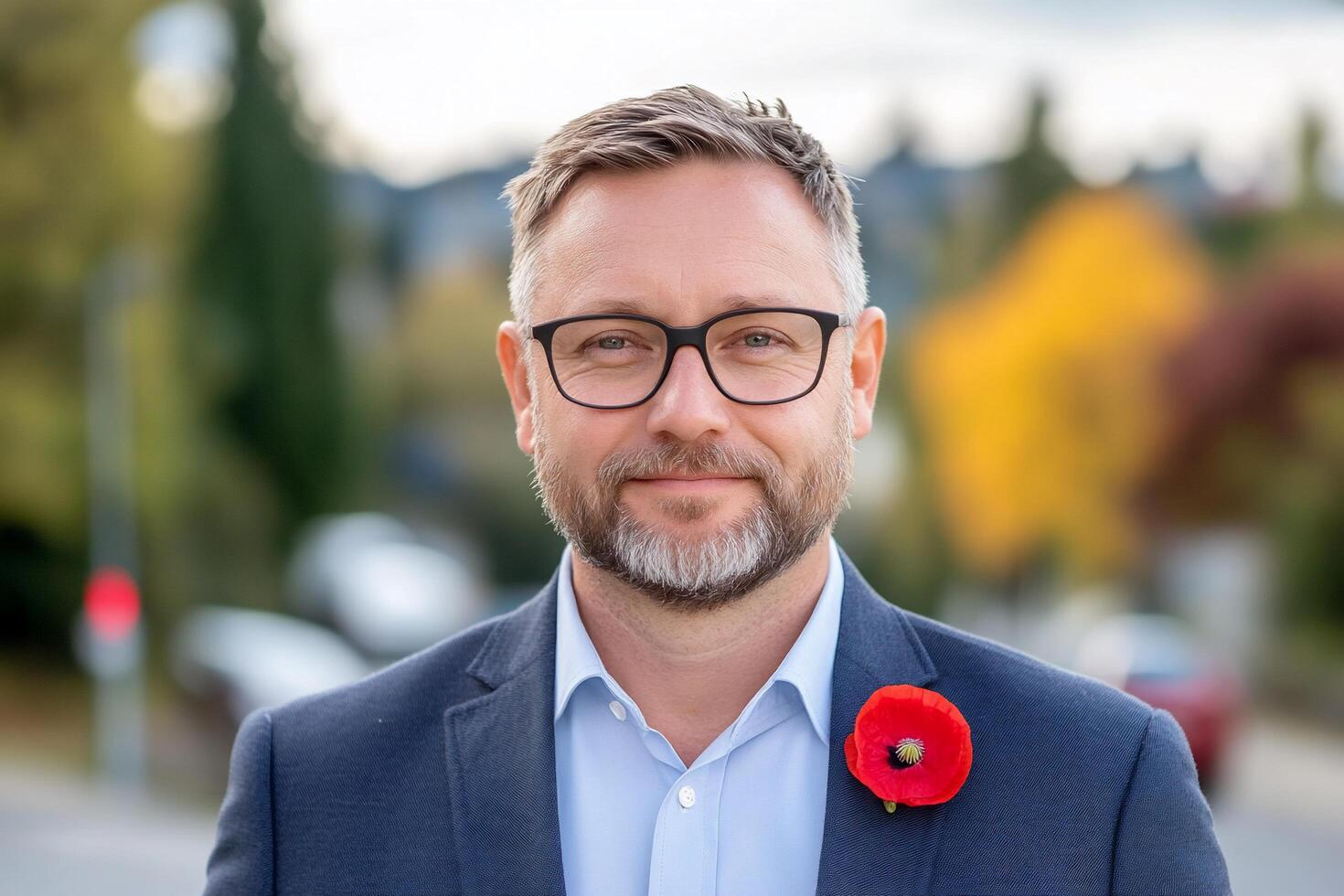A man in a suit with glasses and a poppy flower on his lapel. photo