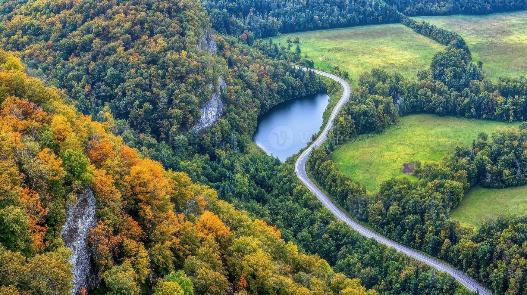 Aerial view of winding road through vibrant autumn forest with river in scenic landscape photo