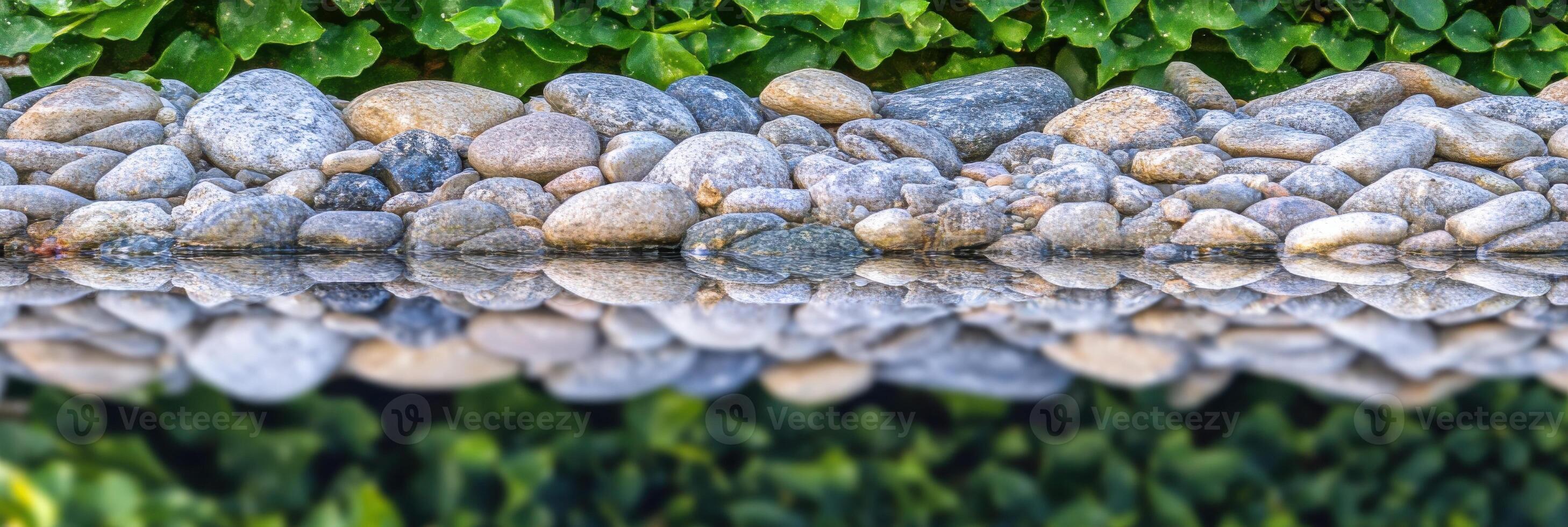 Symmetrical reflection of river stones in calm water with green foliage background photo