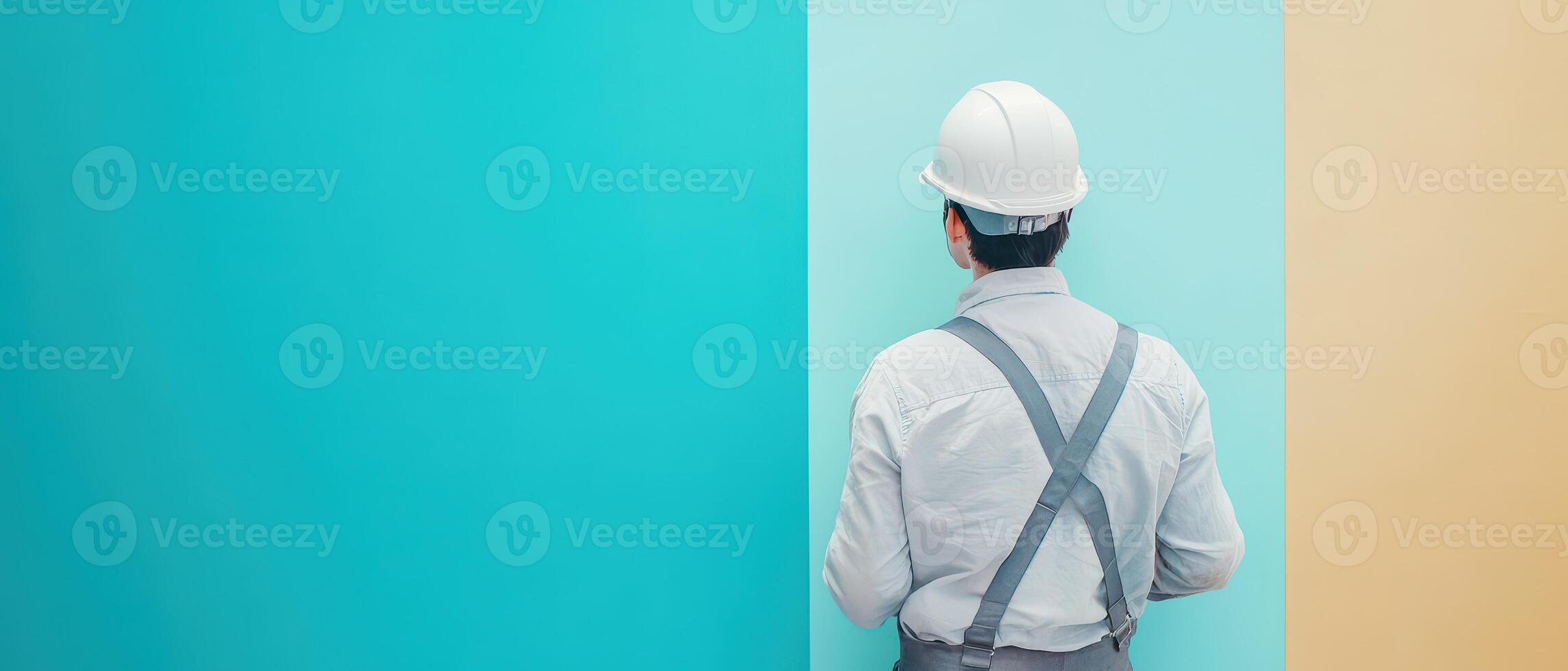 A man in a hard hat and overalls standing in front of a wall photo