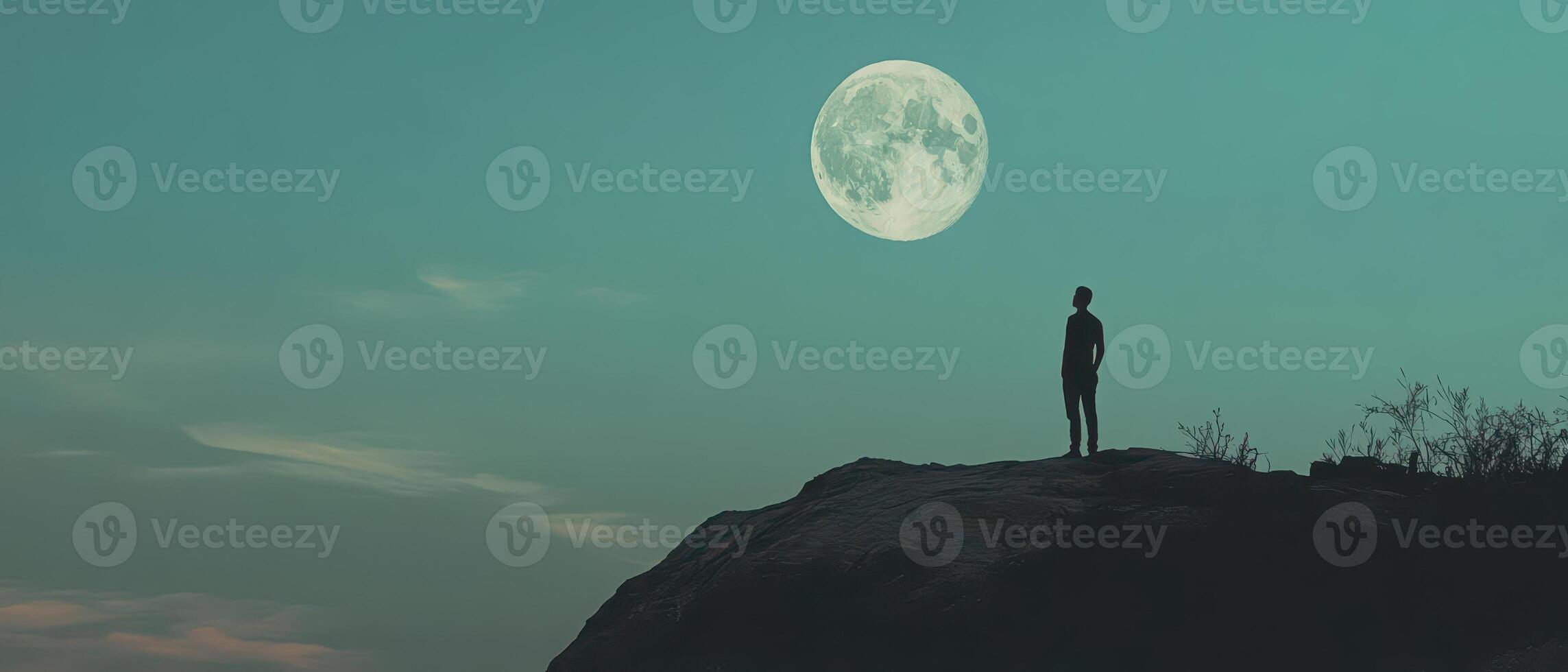 A man standing on top of a mountain with the moon in the background photo