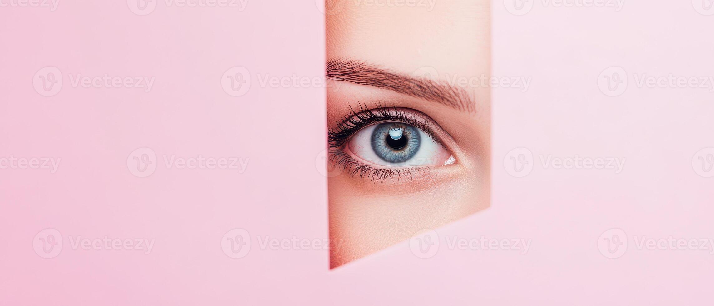 A woman's eye peeking out of a hole in a pink background photo