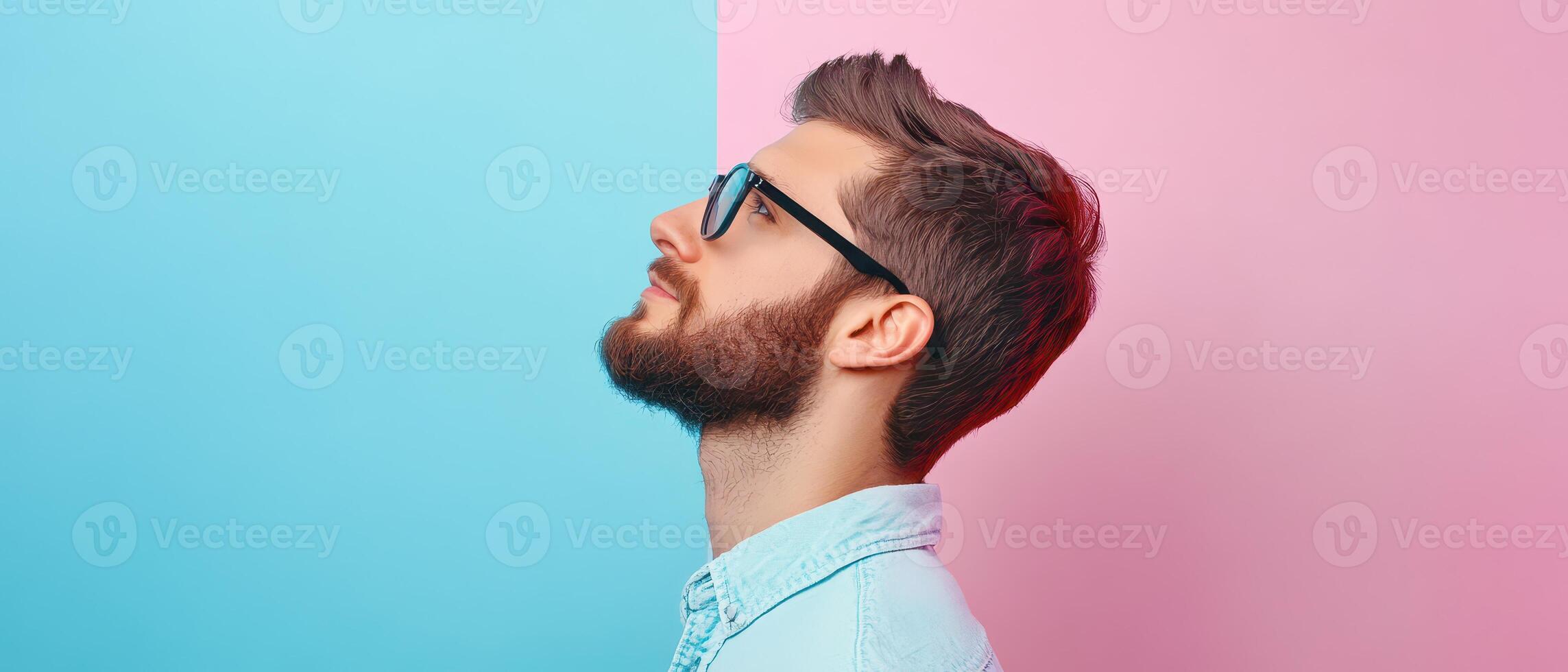 A man with a beard and glasses is looking up at a pink and blue wall photo