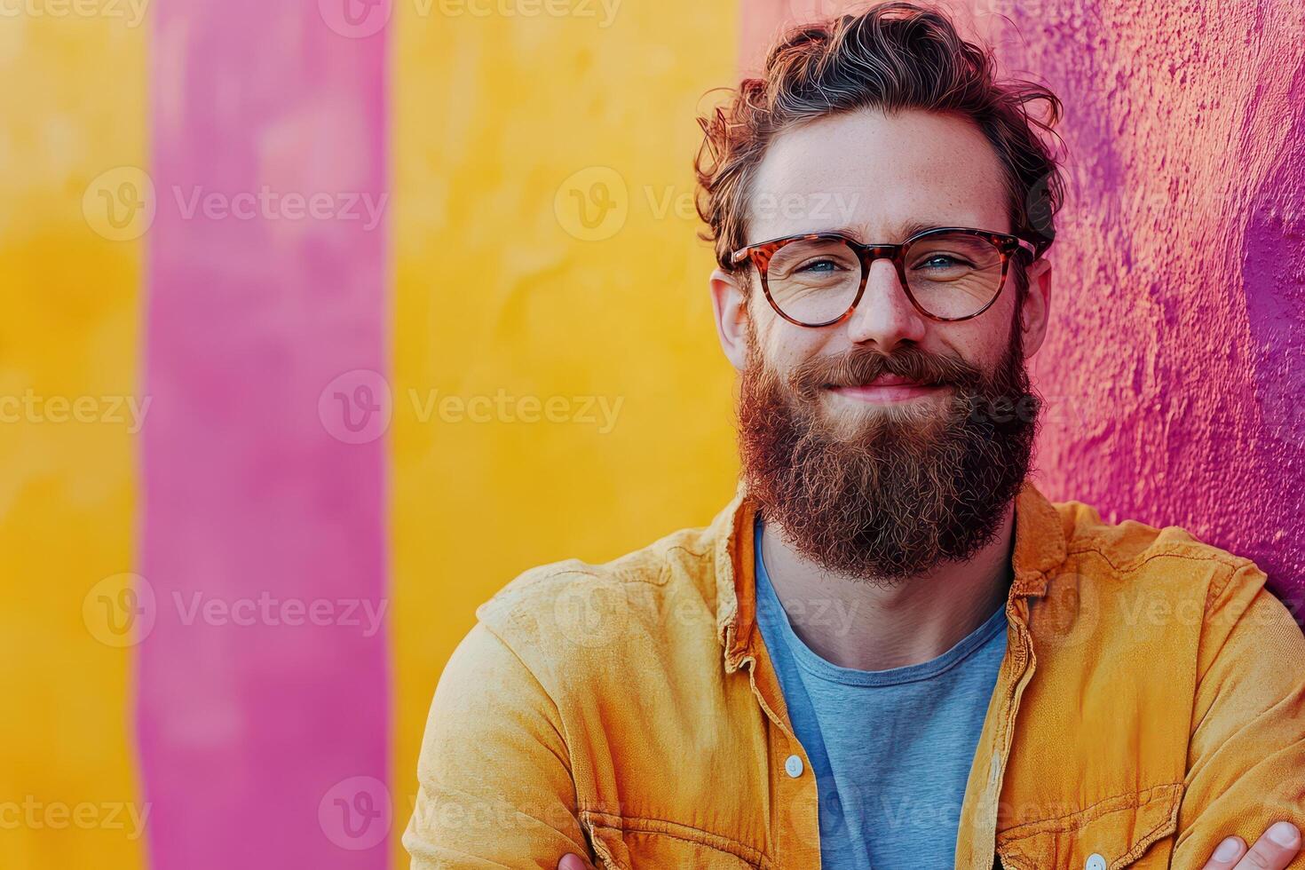 A man with a beard and glasses standing in front of a colorful wall photo