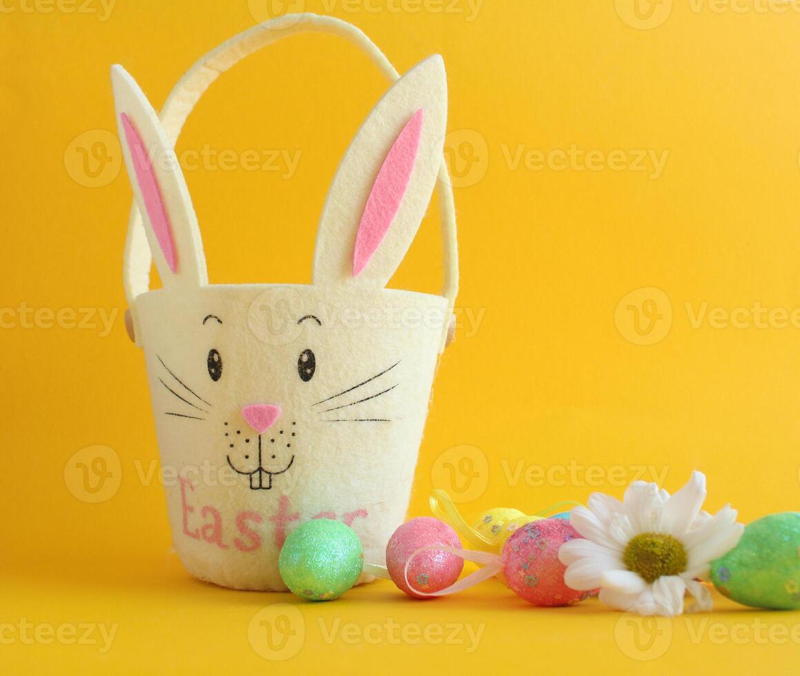 On a yellow background there is an egg basket in the shape of a rabbit and Easter decorative eggs photo
