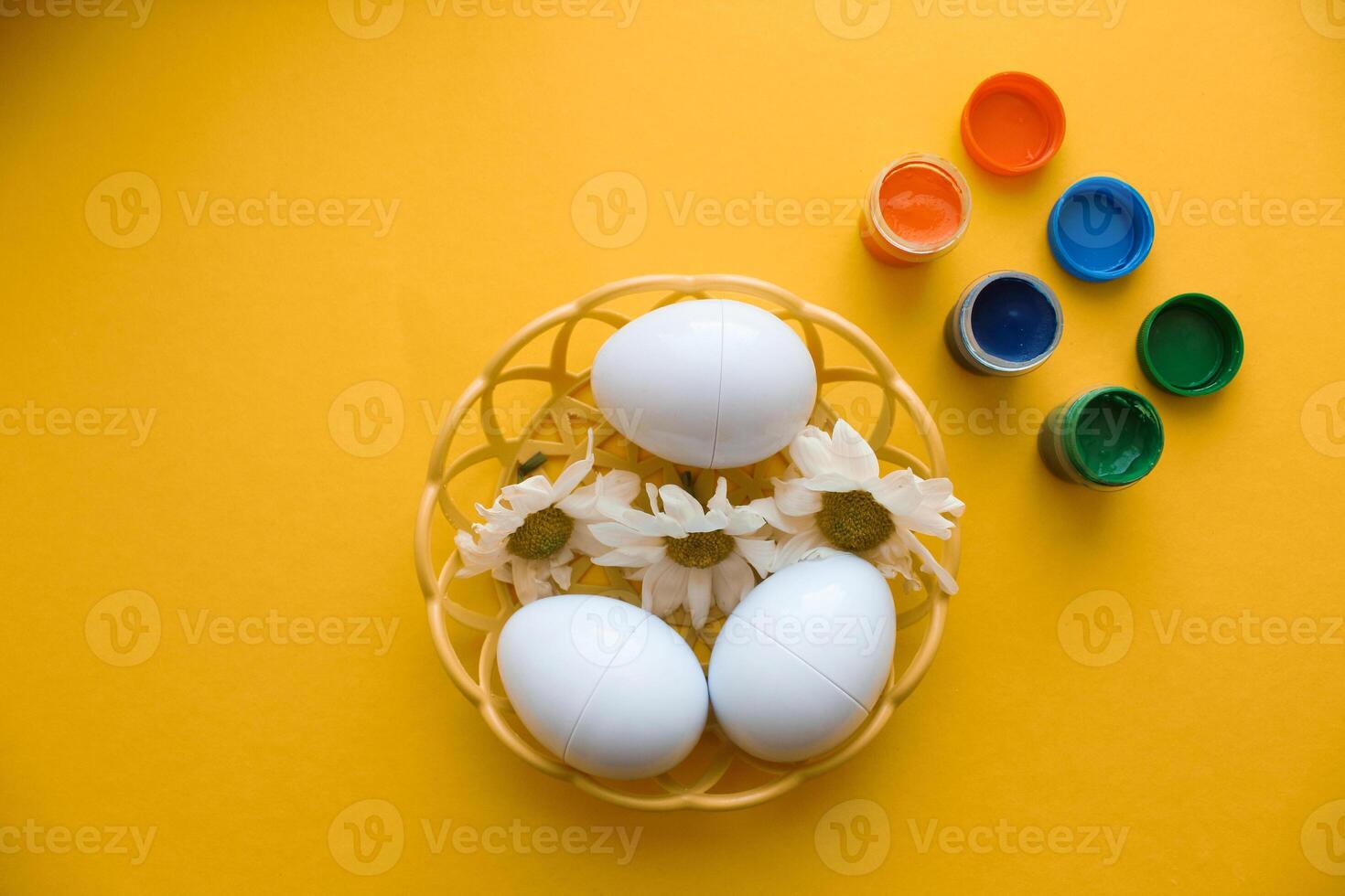 A wicker plate with decorative Easter eggs stands on a yellow background. photo