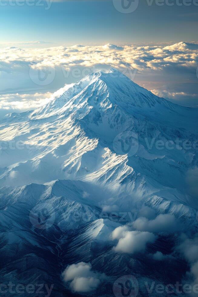 Snowy mountain peak rises above cloud layer. Mountain top with fresh white snow and bright sunlight. Aerial view of mountain range at high altitude. photo