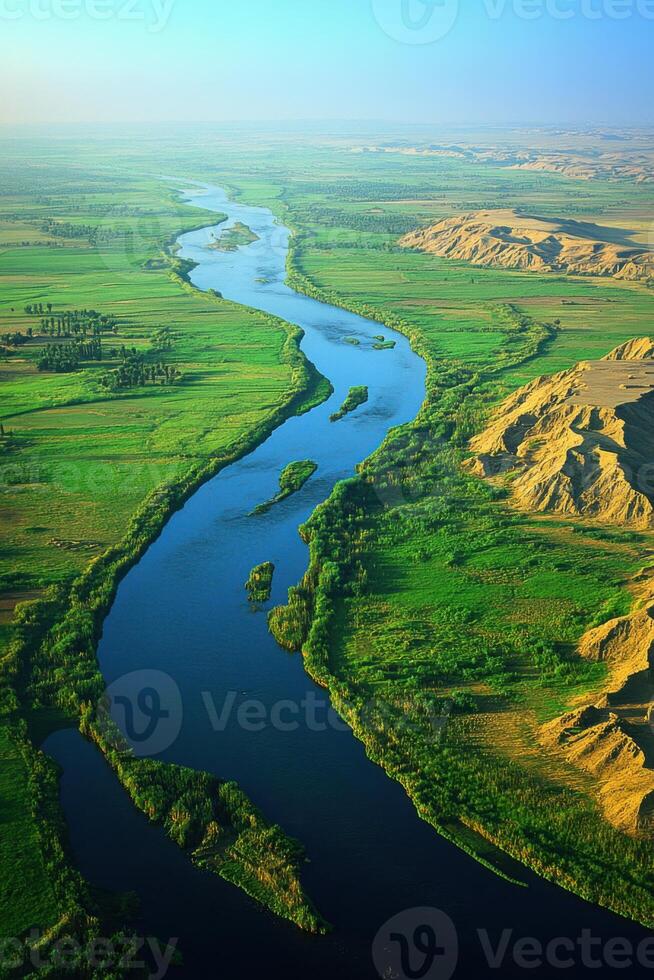 Wide river flows through a green plain. Sand banks rise on the right side. The river curves. A sunny day under a blue sky. photo