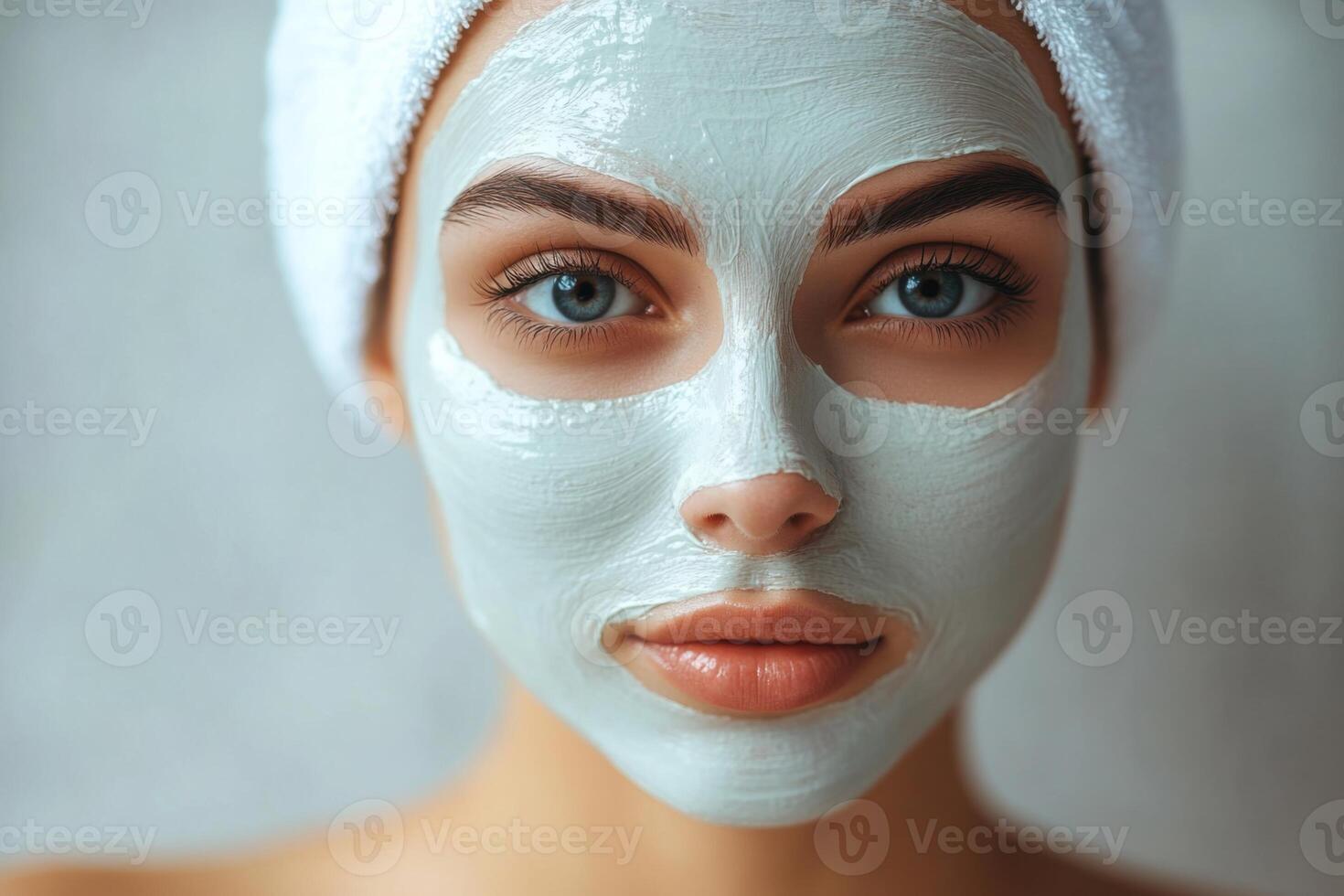 Young woman close up with facial mask and towel on head. Skin care treatment for healthy and beautiful face in spa. photo