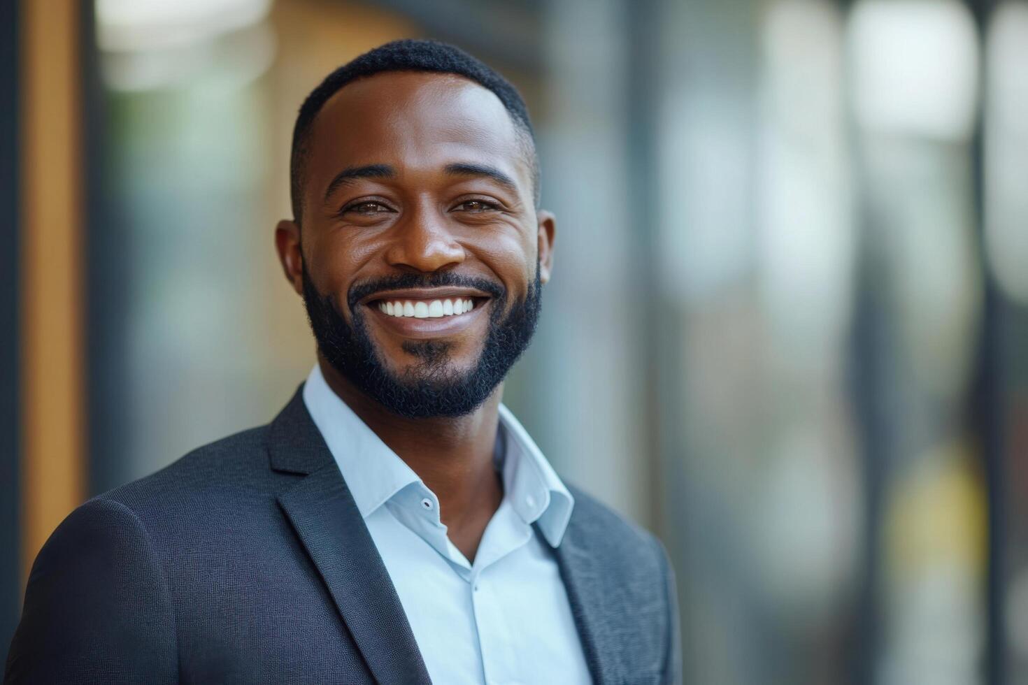 Man smiles looking at camera. Dark suit and light blue shirt in office building. Calm expression with white teeth visible. photo