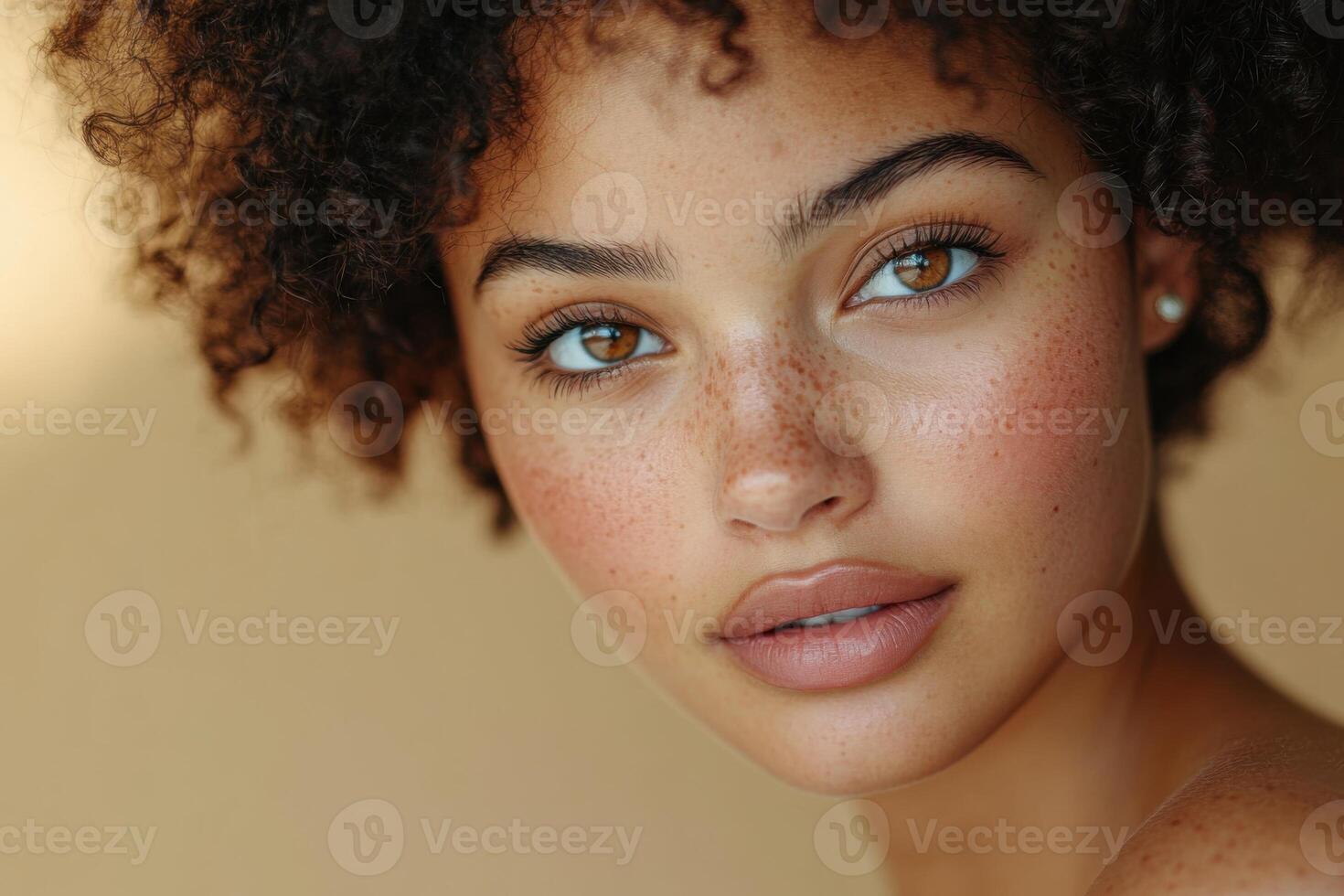 Close up portrait of a young female face with brown eyes and curly hair. She is looking at the camera. Soft light on a beige background. photo