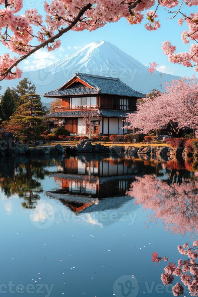 Japanese house near a lake with cherry blossom trees and a snow mountain backdrop reflecting on water in spring on a sunny day photo