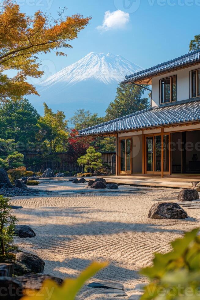 Zen garden with raked sand and rocks near a building and trees. A large mountain with snow stands in the distance under a blue sky. photo