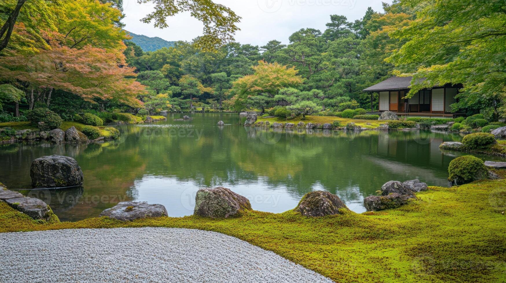 Calm pond reflects autumn trees and a small building in a peaceful garden. Moss covered rocks and gravel add detail in the foreground. photo