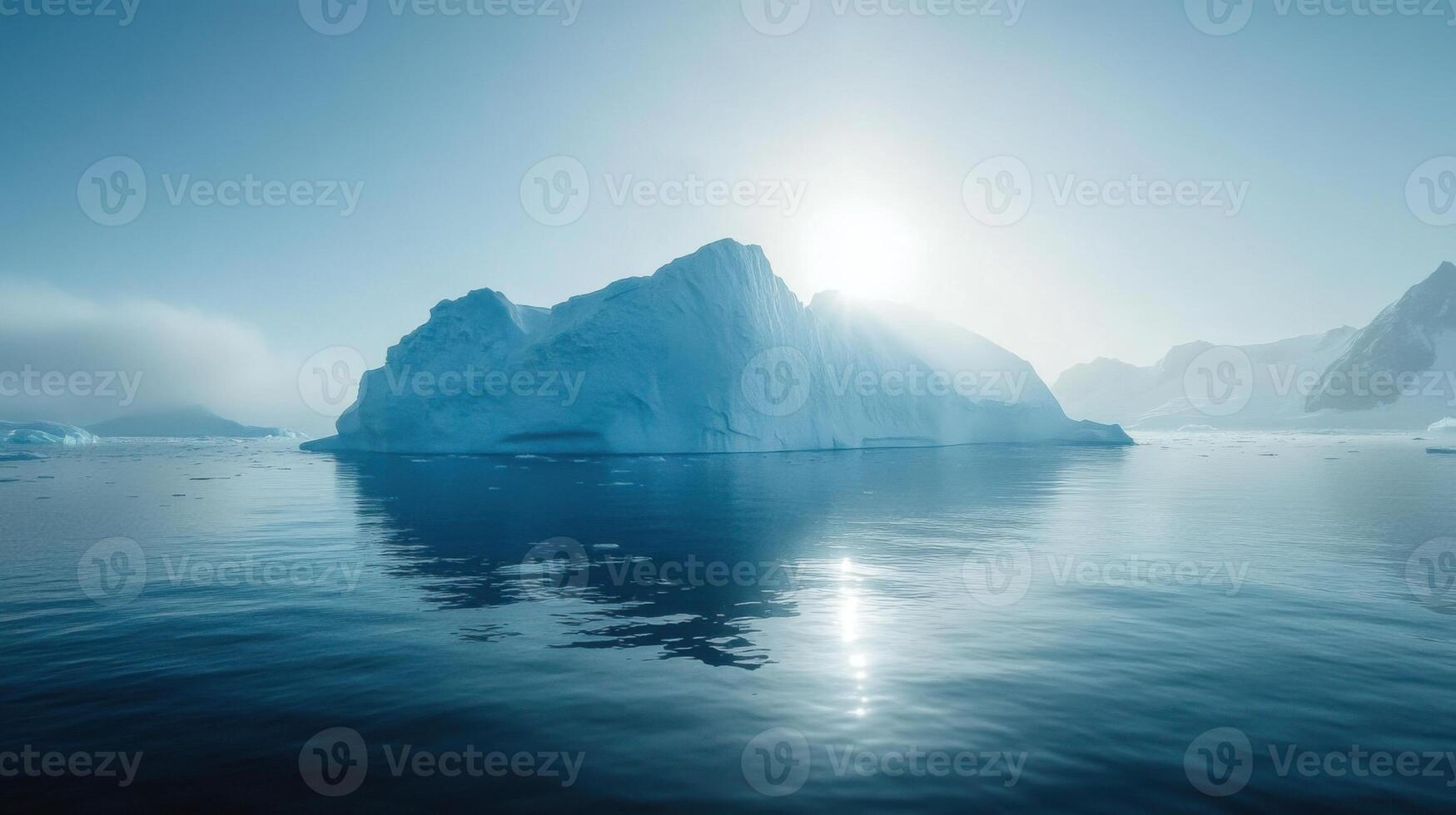 Large iceberg floats in calm arctic ocean water. Bright sun shines behind glacial ice. Mountain peaks visible under a clear blue sky. photo