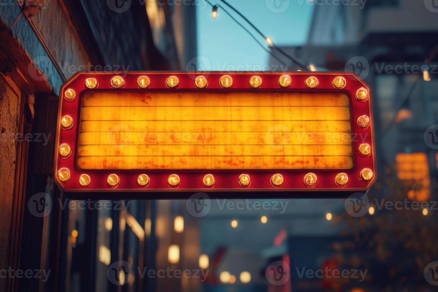 Illuminated sign glows on building exterior. Lights border red frame and illuminate blank yellow panel. Urban background shows city building and hanging string lights. photo