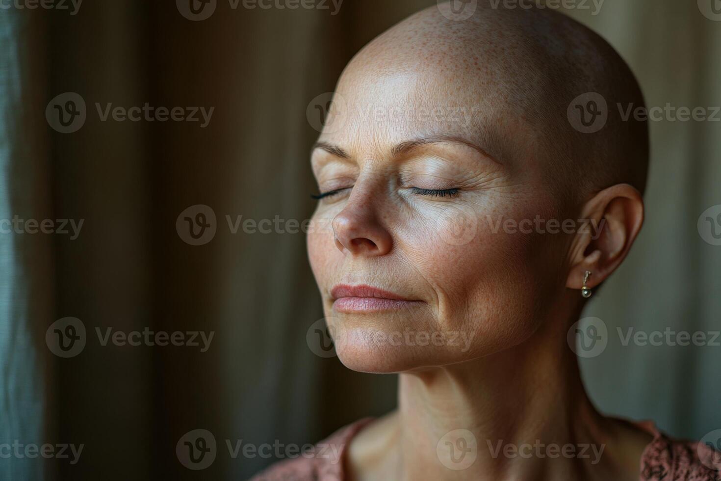 Bald woman with closed eyes meditates indoors. Peaceful face shows tranquility and calmness. Soft light illuminates skin near a window. Serene atmosphere photo