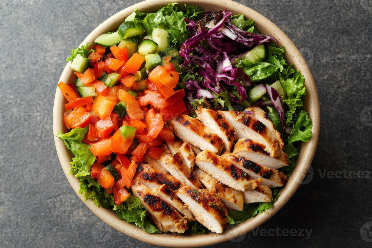 Top down view of a bowl with mixed salad and grilled chicken. Red bell peppers and sliced cucumbers with red cabbage on lettuce. photo