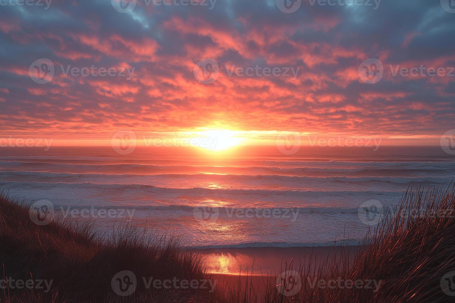 Bright sunset over ocean horizon. Waves gently rolling onto sandy beach. Grasses in foreground. Clouds reflect orange and red light. photo