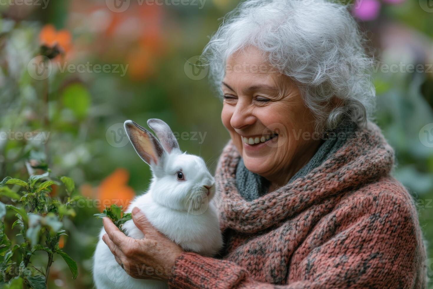 Woman holds white rabbit in garden. She smiles in happiness. Flowers and foliage in background. Peaceful moment. Natural light. Close up. photo